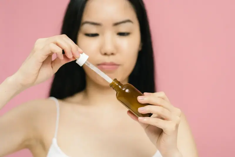 Woman holding an amber serum bottle and dropper against a pink background