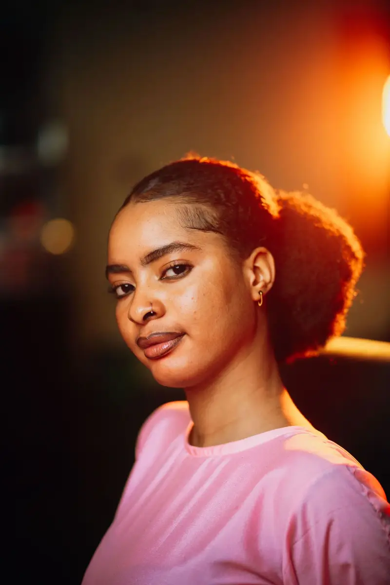 Young woman with glowing skin in a pink tee under warm evening light