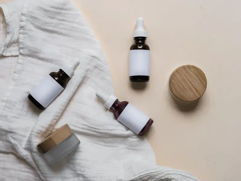 Glass skincare bottles with blank labels resting on a textured fabric
