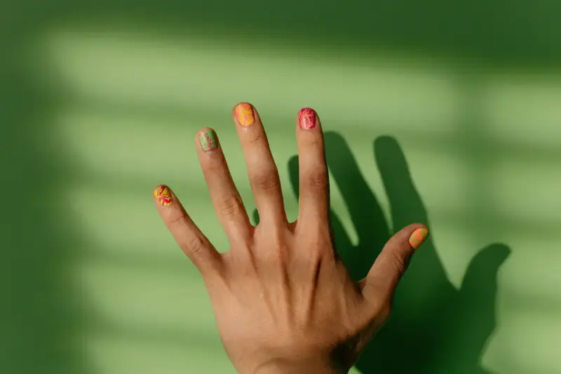 Hand with intricate nail art casting shadows on a green surface