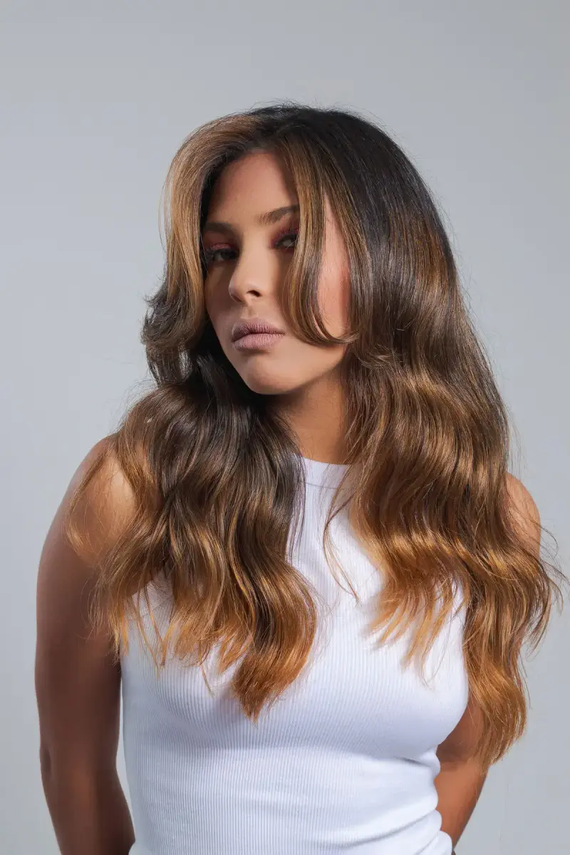 Woman with long brunette balayage waves in a white top, studio portrait