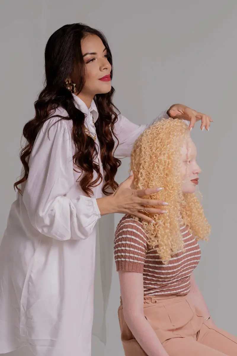 Hairstylist with long dark waves styling a model's voluminous blonde curls