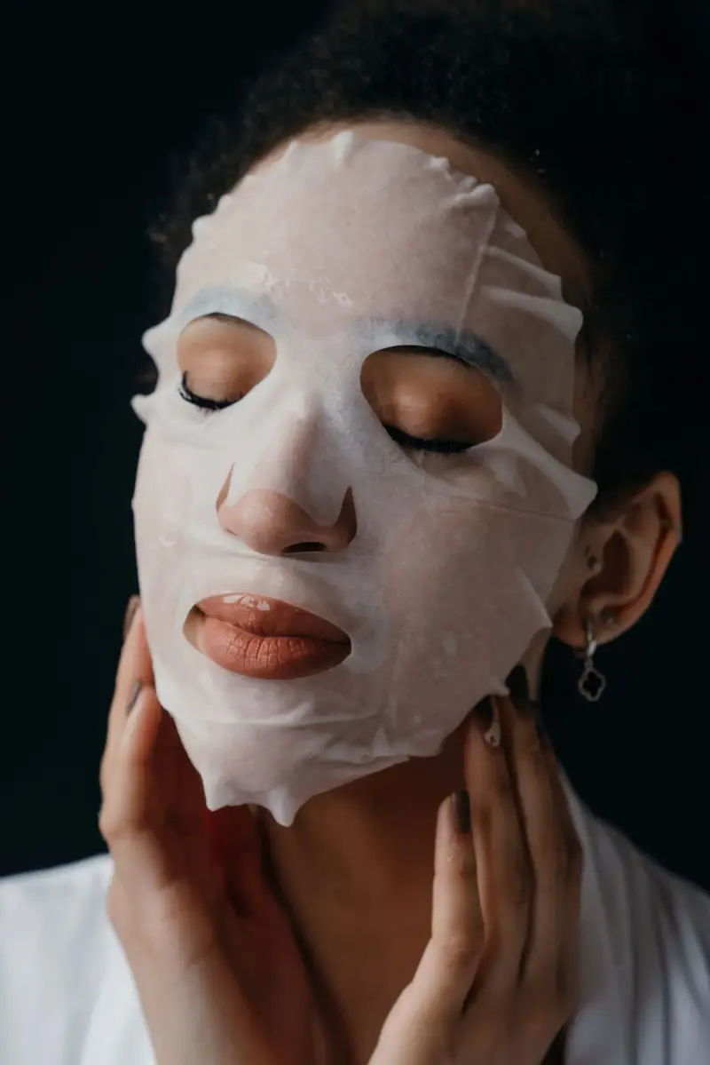 Woman wearing a hydrating sheet mask against a dark background