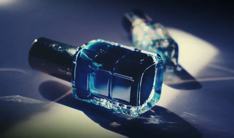 Single bottle of blue nail polish casting a reflection on a white surface
