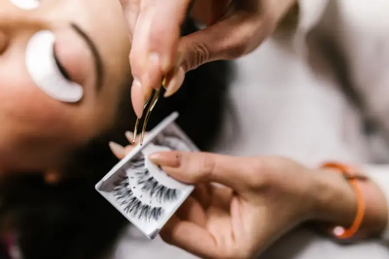 Hand holding tweezers with a strip of false eyelashes