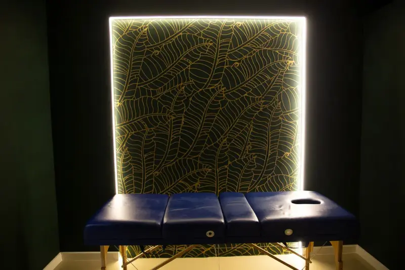 Treatment room with a blue massage table and an illuminated wall panel
