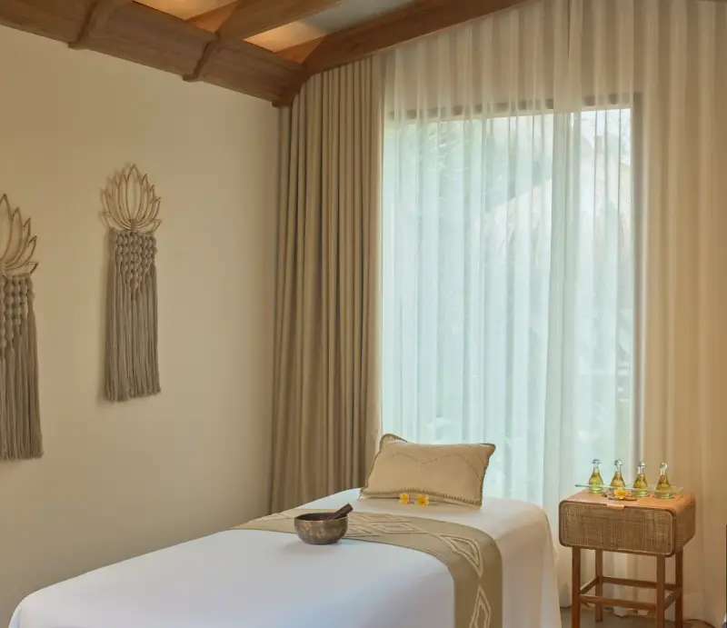 Spa treatment room with massage table, singing bowl, oil bottles and sheer curtains