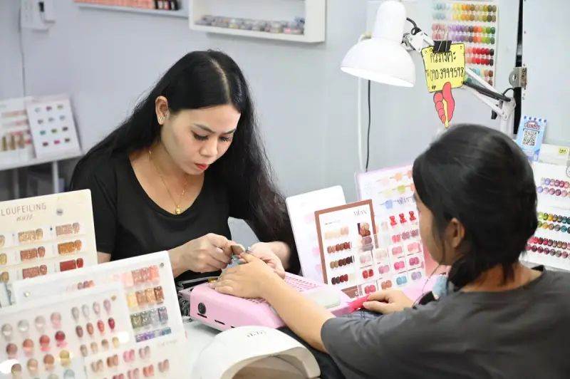 Nail technician filing a client's nails at a workstation surrounded by gel color charts