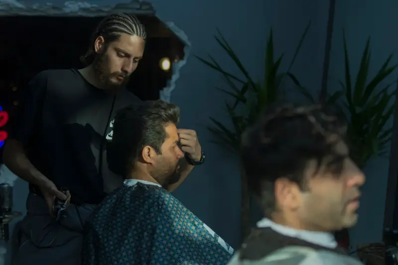 Barber trimming a seated client's hair with clippers in a dimly lit salon
