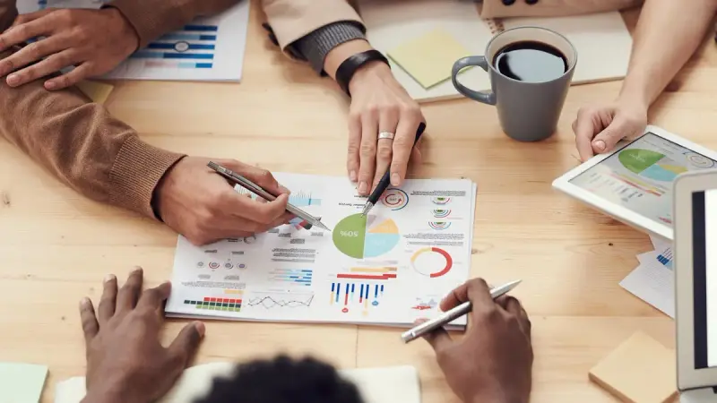 Hands pointing at printed charts and a tablet during a data meeting