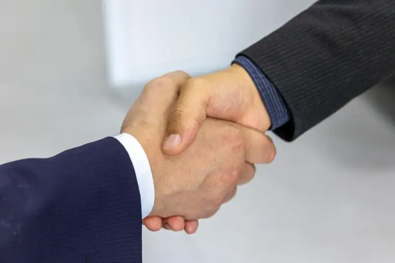 Two businessmen shaking hands across a meeting table