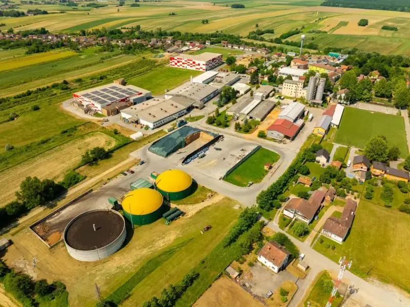 Aerial view of a farm village with a biogas plant, its two yellow-domed digesters beside a round tank