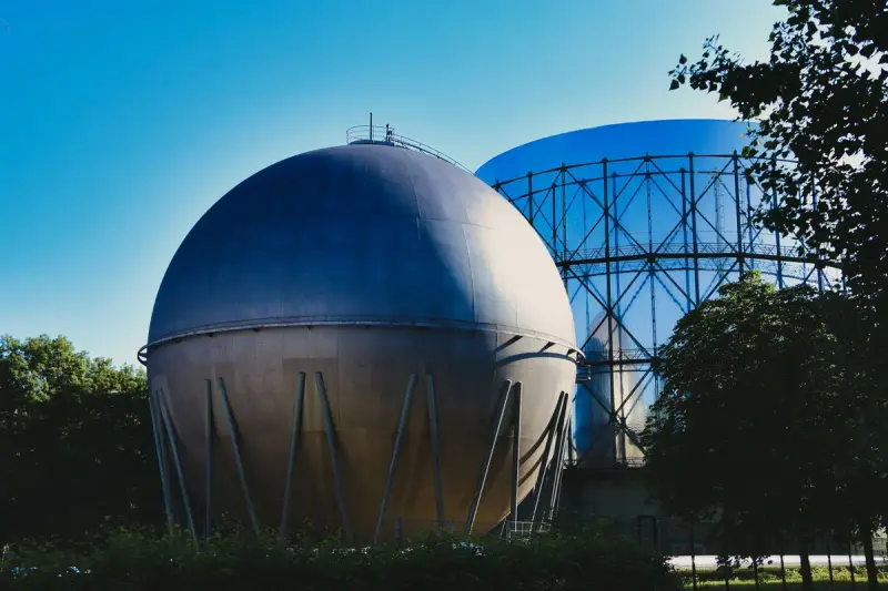 Spherical steel gas holder beside an older gasometer frame under a blue sky