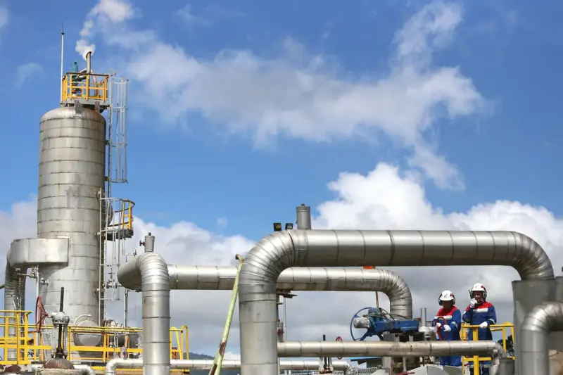 Two engineers in hard hats walking past stainless steel pipes and a column at a gas plant