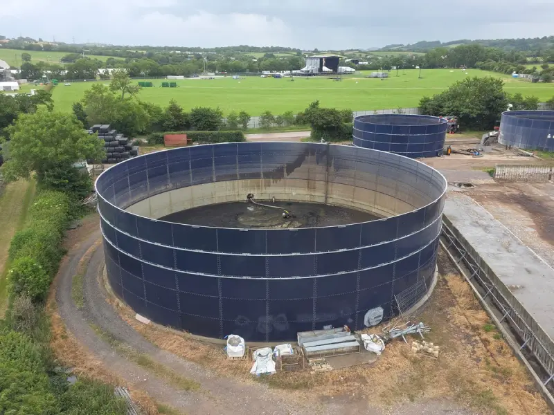 Large dark blue steel digester tank under construction beside a green field