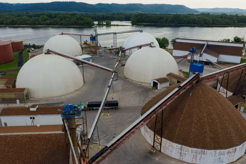 White domed storage structures and conveyors at an industrial site beside a river