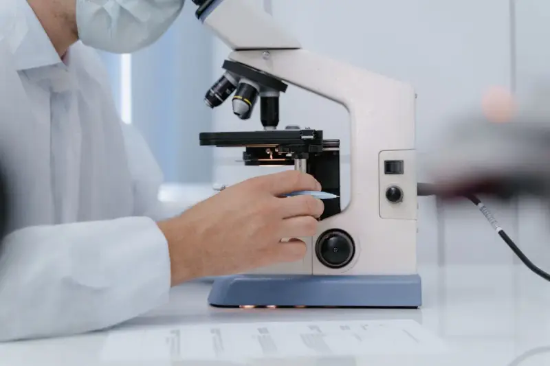 Researcher in a lab coat adjusting the focus of a white research microscope