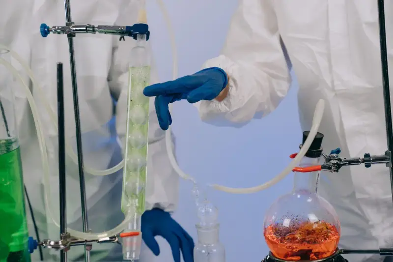 Gloved hands adjusting a glass column and tubing over a heated flask in a lab