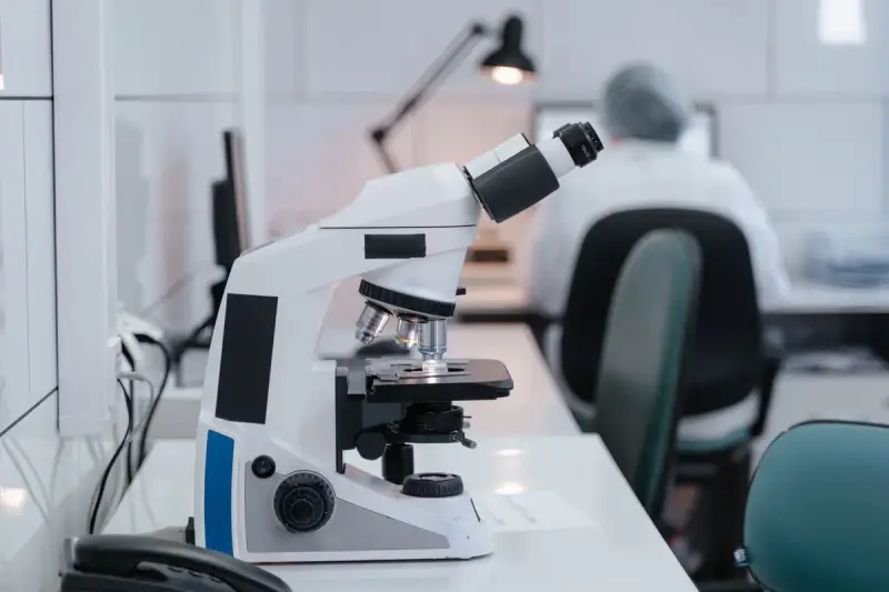 Microscope on a white lab desk with a scientist working in the background