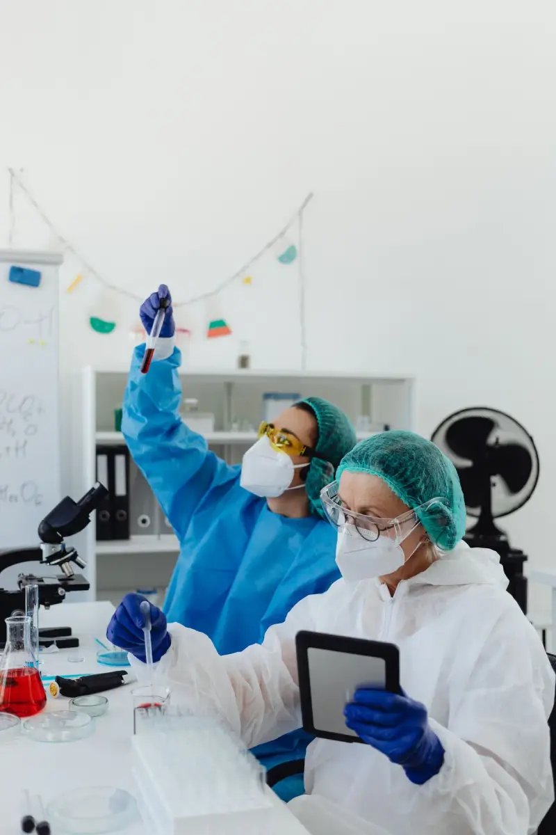 Two scientists in protective gear checking a sample tube and a tablet in a lab