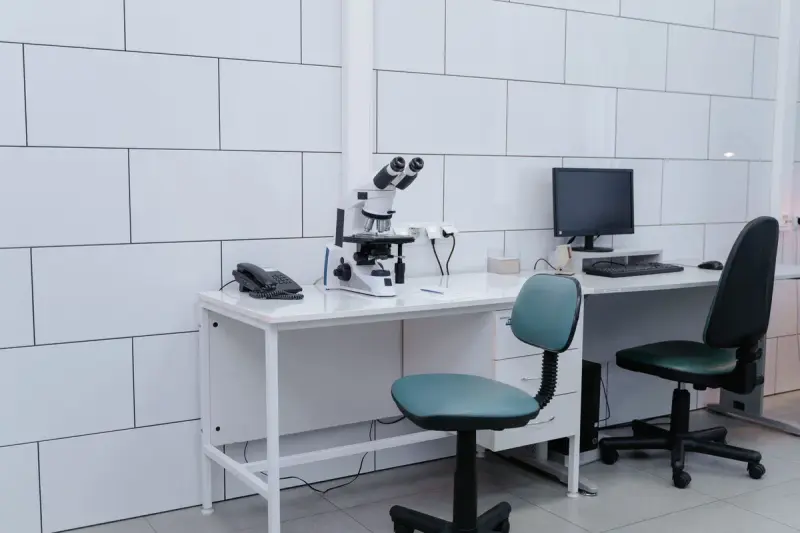 Clean white laboratory with microscopes, monitors and a scientist working at the far bench