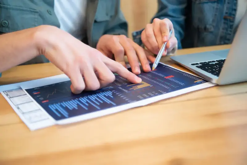 People discussing data charts beside a laptop