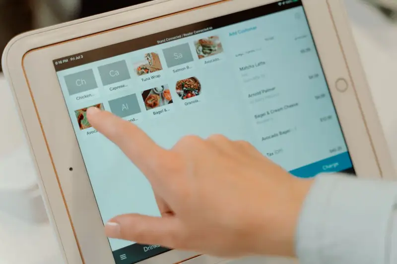 Finger tapping menu items on a tablet point-of-sale screen in a restaurant