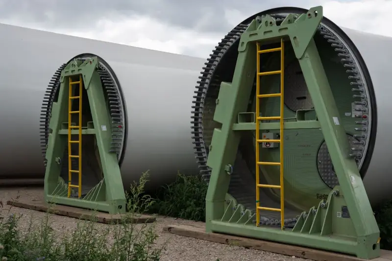 Two composite wind turbine blade roots resting in green steel transport frames outdoors
