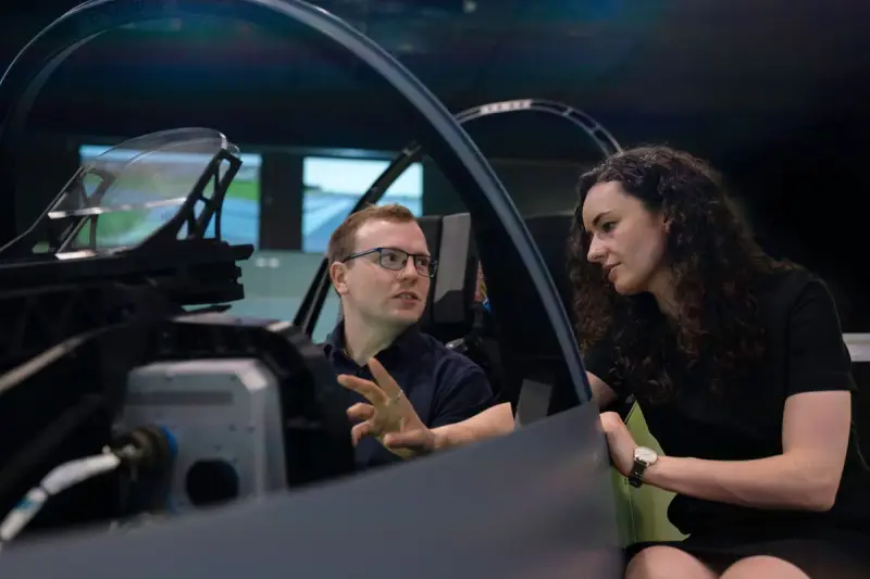 Two engineers talking beside an open aircraft cockpit mockup