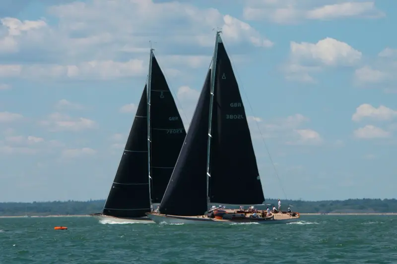 Two racing yachts with black sails heeling on open water under a blue sky
