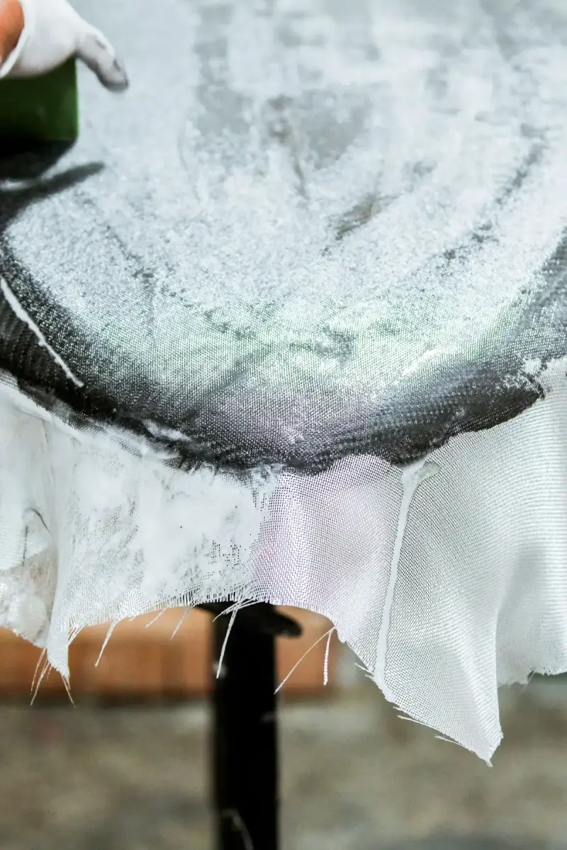 Close view of resin-wetted fiberglass cloth laminated over a board with frayed cloth at the edge