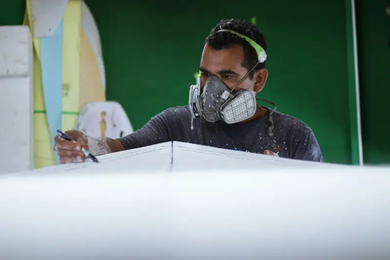 Worker in a respirator marking a foam blank before fiberglass layup in a workshop