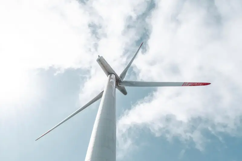 Low view of a wind turbine with long white blades against bright clouds