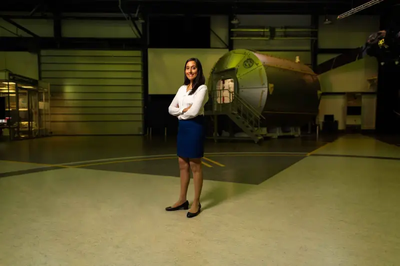 Female engineer standing with arms crossed in a hangar beside a spacecraft module
