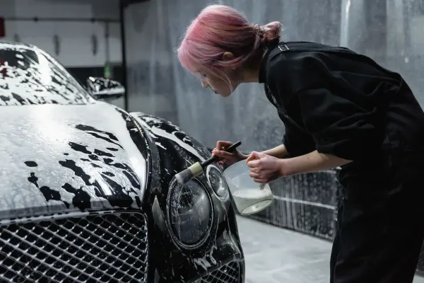 Woman cleaning a black car headlight with a detailing brush