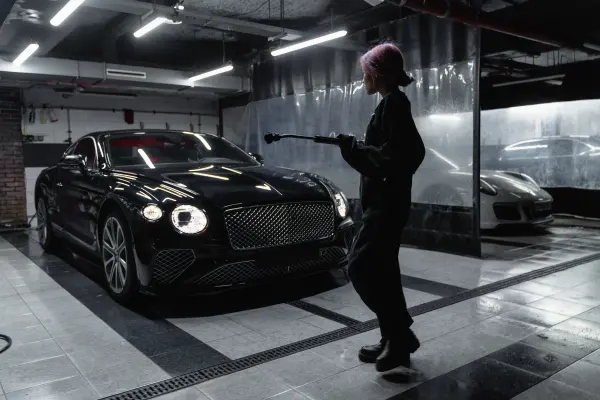 Woman holding wash equipment beside a black car in a garage
