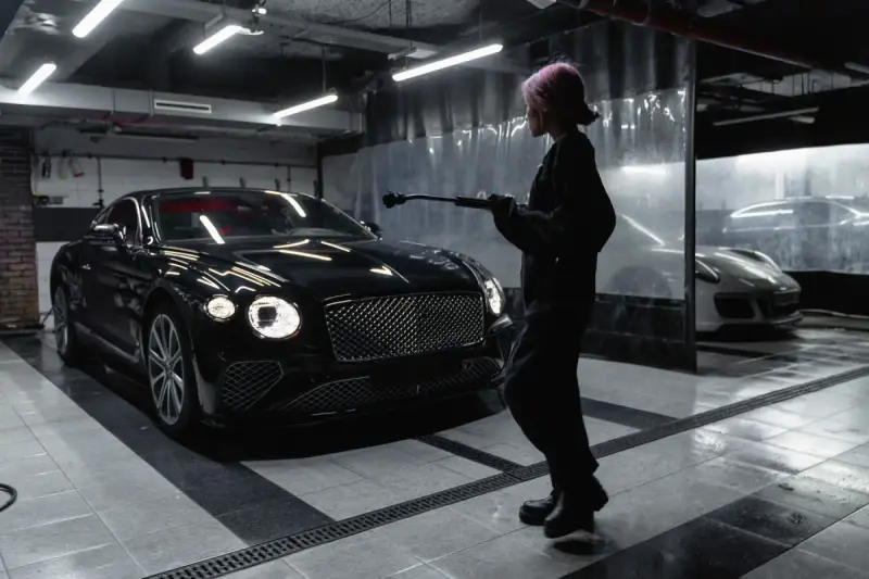 Woman holding wash equipment beside a black car in a garage
