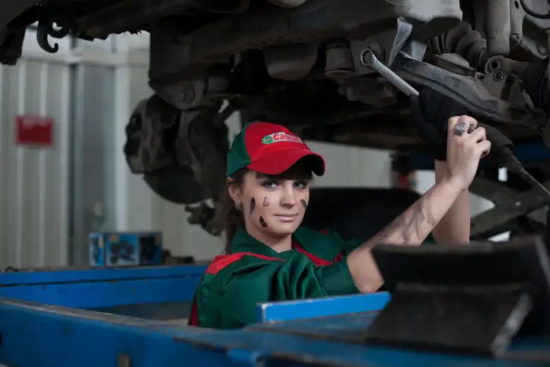 Woman mechanic holding a wrench while working on a car in an automotive workshop