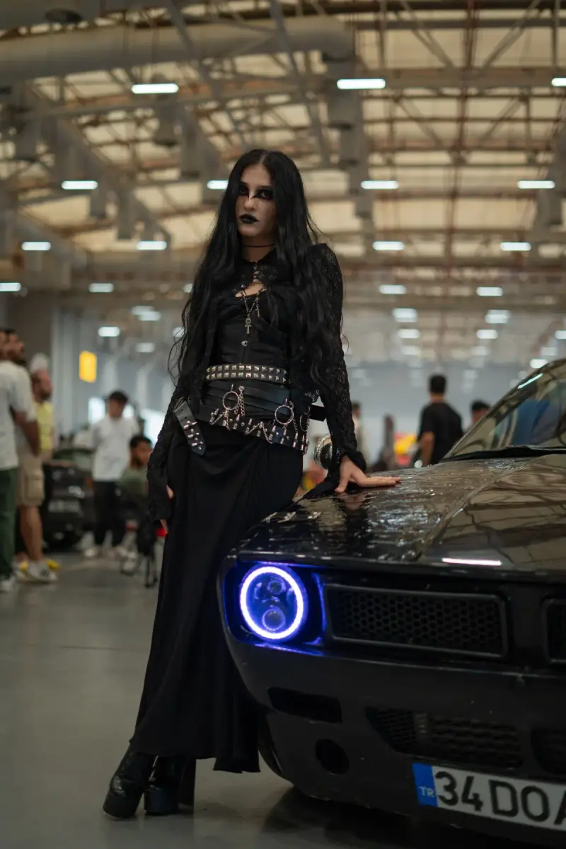 An adult woman beside a muscle car at an indoor automotive exhibition