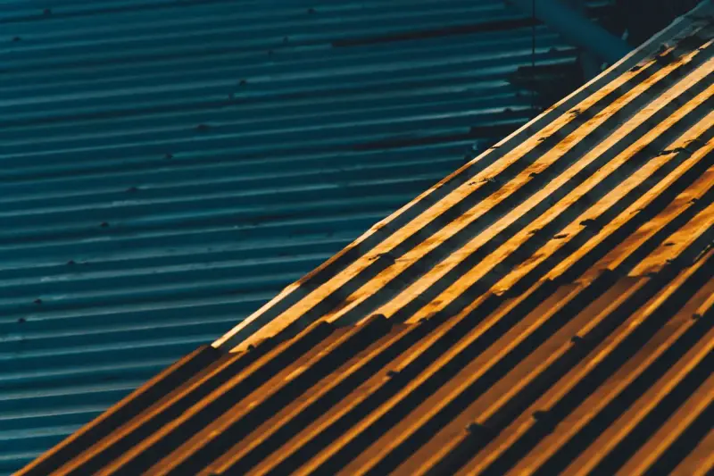 Low sun raking across corrugated sheet metal roof panels in teal and rust