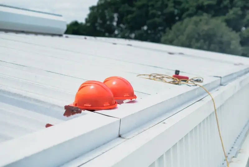 Two orange hard hats and a safety line resting on a white standing-seam metal roof