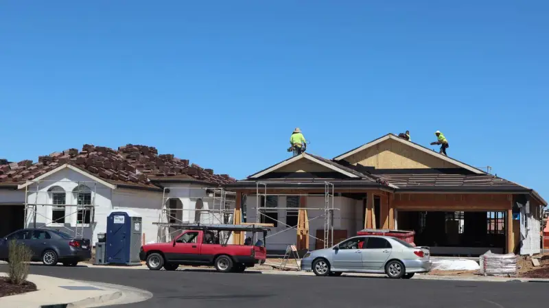 Roofers working on the roof of a new suburban home with trucks parked out front