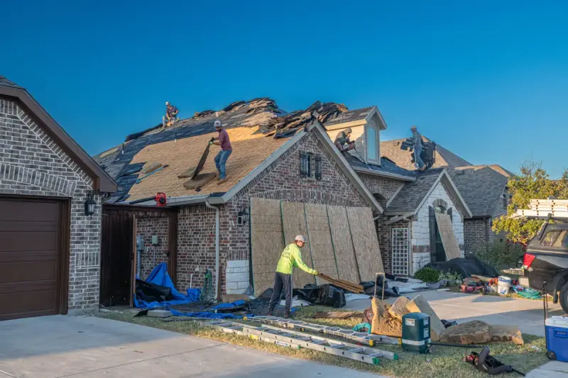 Roof replacement under way on a brick house, with decking boards and tools in the driveway