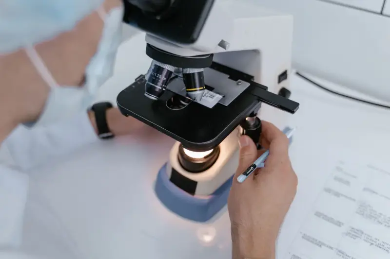 Close view of a gloved researcher adjusting a lit microscope stage