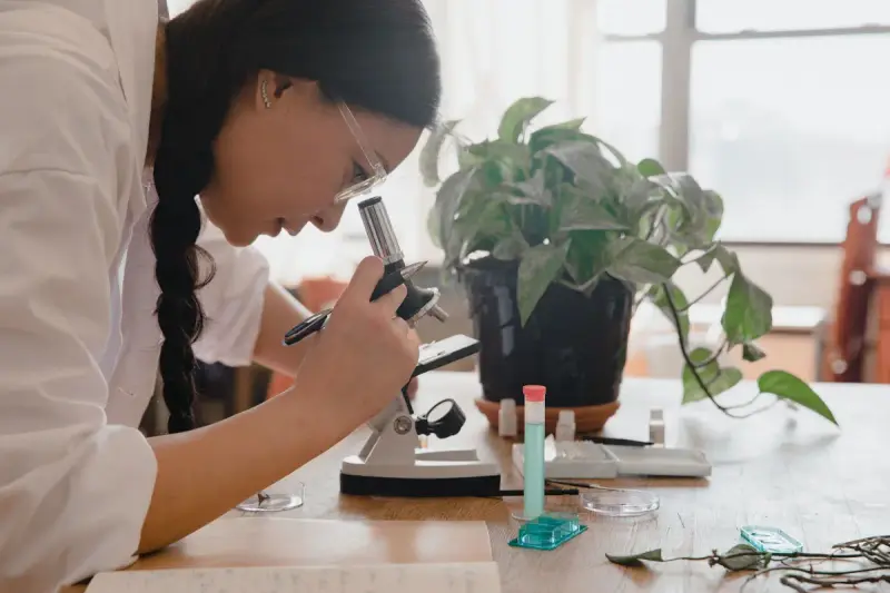 Young female scientist leaning over a microscope in a bright lab