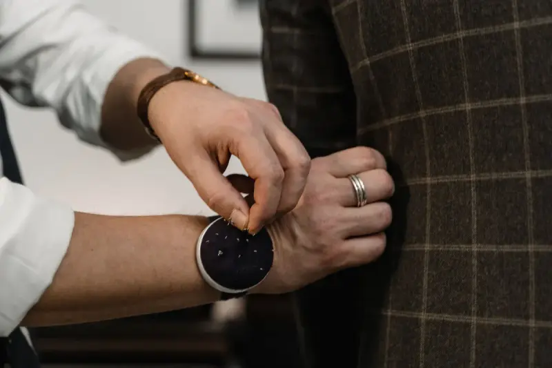 Tailor's hands checking a button on a brown windowpane check blazer