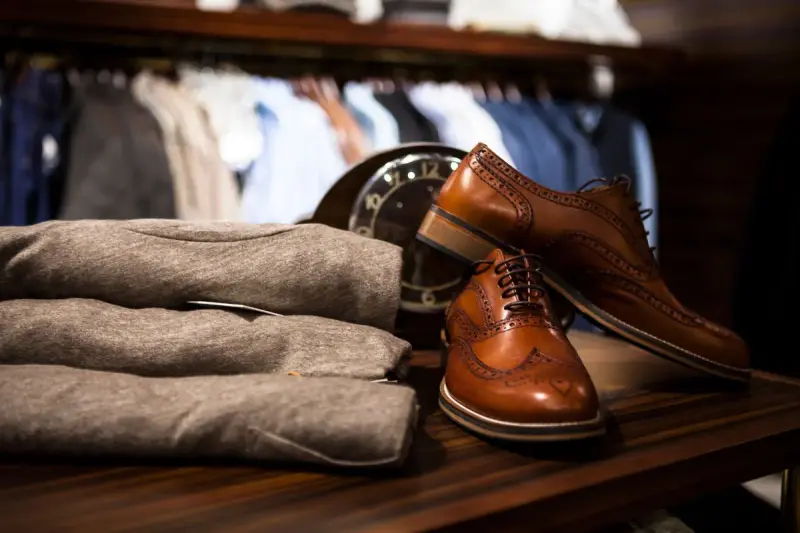 Brown leather wingtip shoes beside grey knitwear on a wooden table