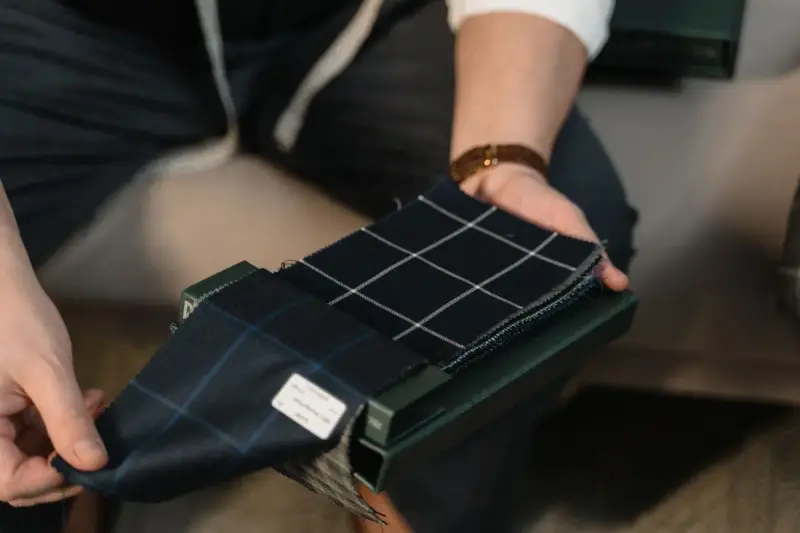 A tailor's hands fan out checked fabric swatches for a bespoke suit