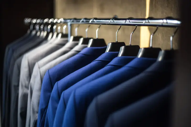 A neat row of dark suits hanging side by side on a rail