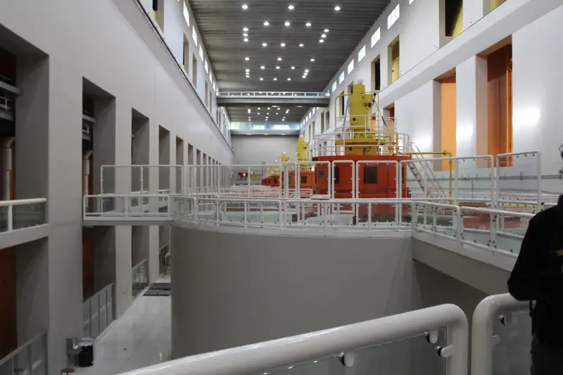 Row of hydroelectric generator units along the floor of a powerhouse hall